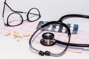 Glasses, pills, and a stethoscope on top of EKG results